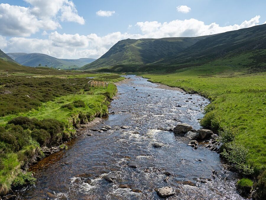 Scenic view of a river winding through a valley with mountains in the background, located in Cairngorms National Park, Scotland.