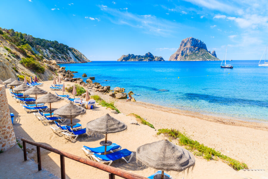 Scenic view of Cala d'Hort beach, showcasing sunbeds, umbrellas, and vibrant blue sea on Ibiza island, Spain