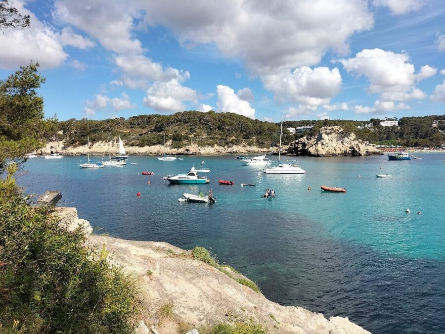 Boats are docked in the water near a rocky shore at Cala Galdana, Menorca, showcasing a serene coastal panorama.