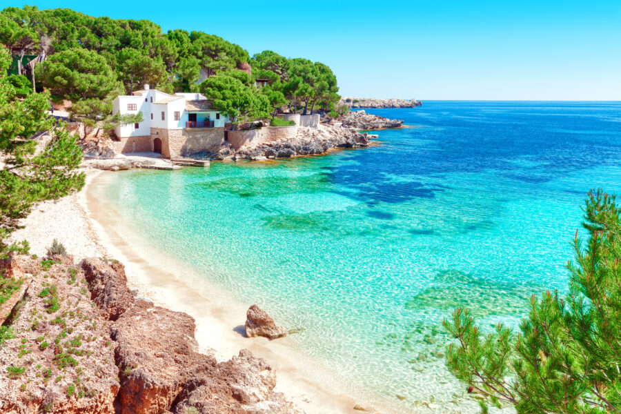 Cala Gat in Mallorca, Spain, features a serene beach with turquoise waters and rocky cliffs under a clear blue sky