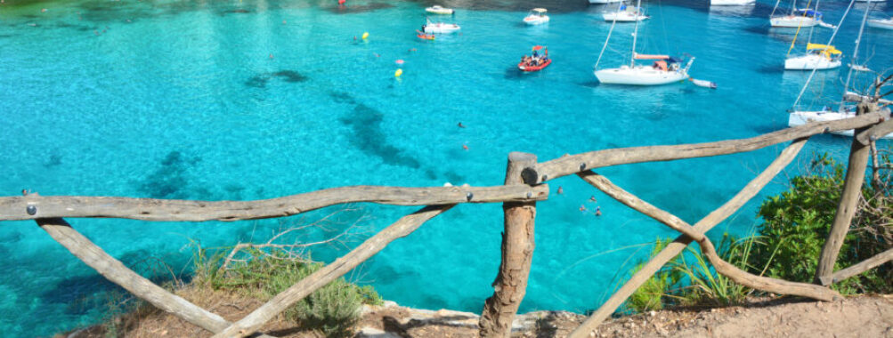 Scenic view of Cala Macarella bay in Menorca, featuring vibrant turquoise water and several boats anchored.