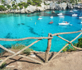 Scenic view of Cala Macarella bay in Menorca, featuring vibrant turquoise water and several boats anchored.