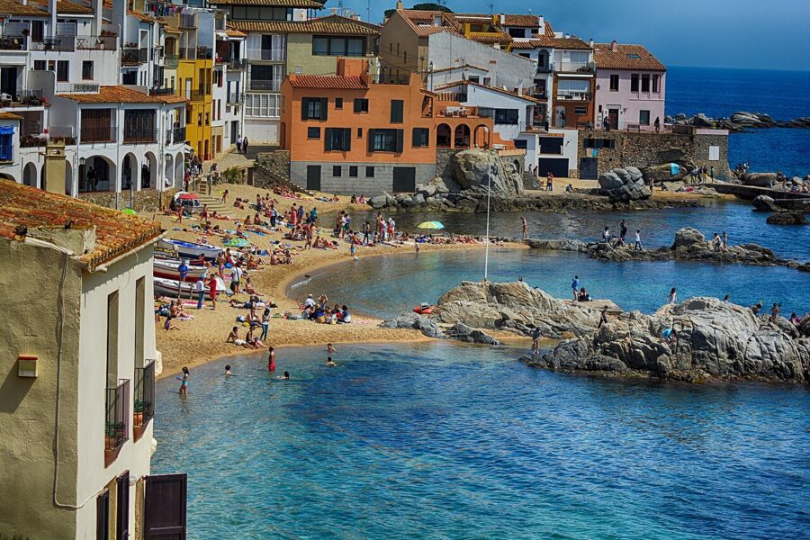 Crowded Calella de Palafrugell beach scene, featuring numerous visitors and expansive water under a clear sky.