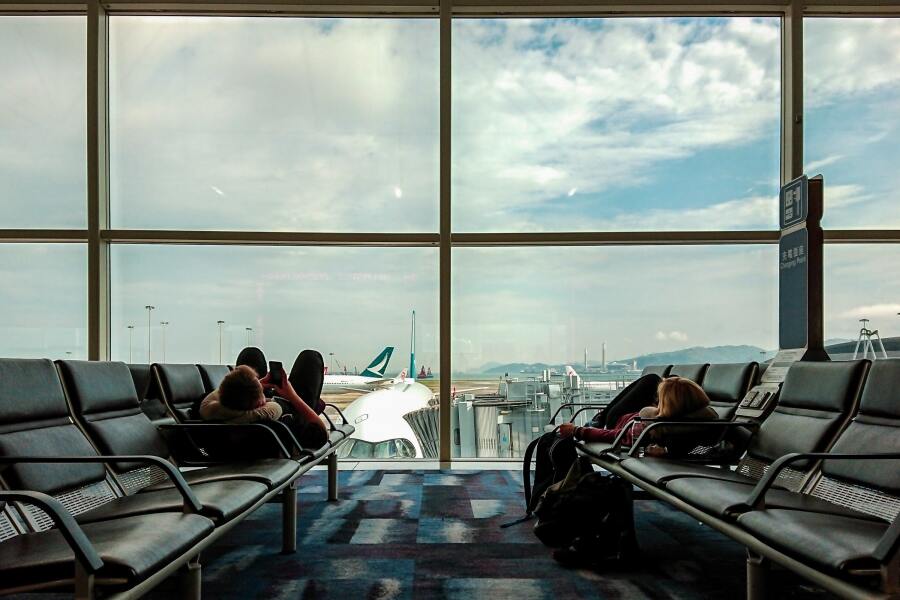 Airport terminal with passengers relaxing, vibrant carpet, panoramic view of planes and mountains.
