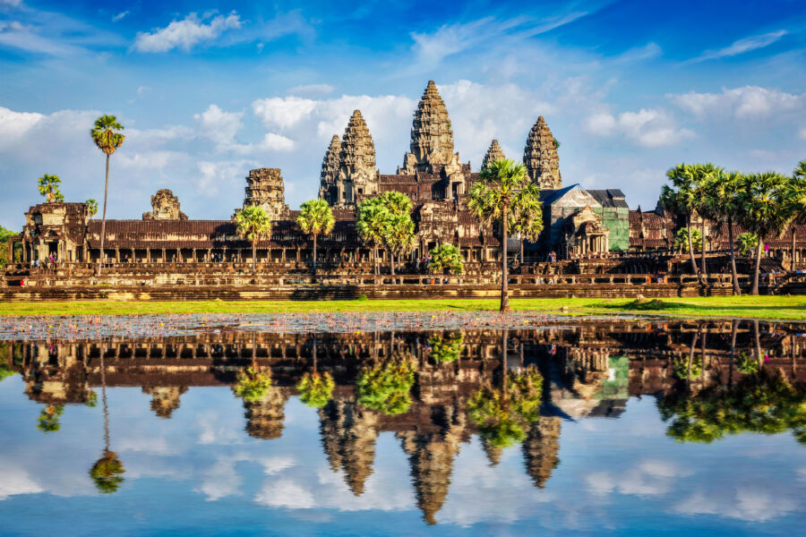 Angkor Wat temple complex in Cambodia, reflecting in a river under a clear sky, showcasing its stunning architecture