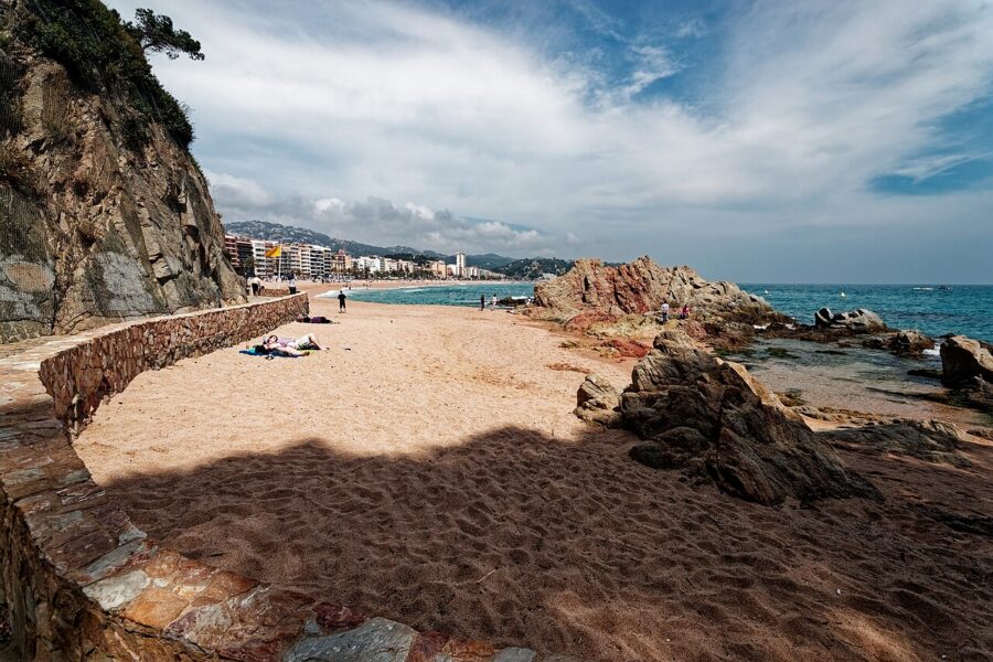 Sandy beach on the Costa Brava, Spain, with people relaxing on the sand near the Camí de Ronda Hiking Trail.