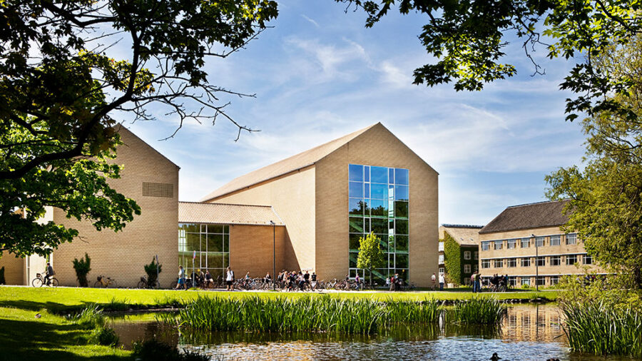 Aarhus University campus buildings and pond with students and bicycles on a sunny day.