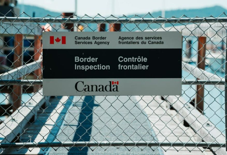 Canada Border Services Agency sign at inspection area, bilingual, with Canadian flag and security fence.