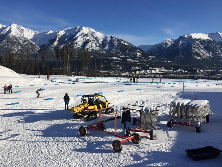 Scenic view of a snow-covered ski slope in Canmore, Canada, with a snowmobile and cart resting on the snow.