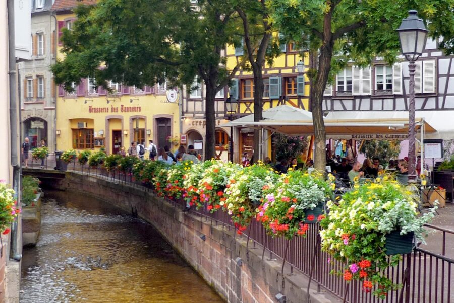 Colmar Little Venice canal with flower-lined banks, riverside cafe, timber-framed houses, Alsace, France.