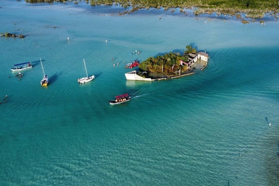 Aerial view of a small island in Canal de los Piratas, Bacalar, Mexico, with several boats floating in the turquoise water.