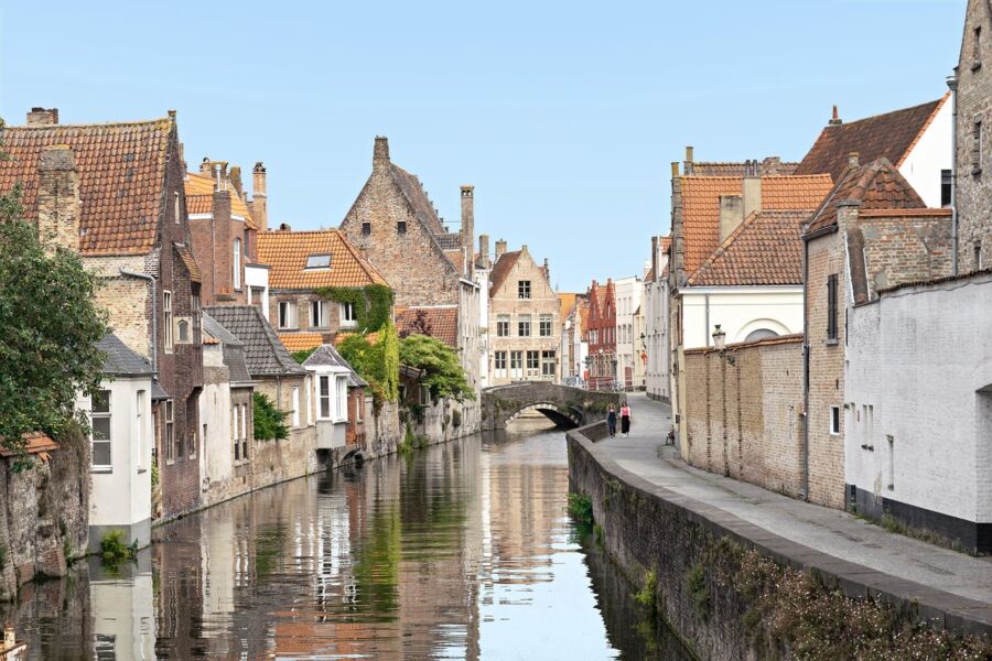 Historic European canal scene with quaint architecture, arched stone bridge, and lush greenery.