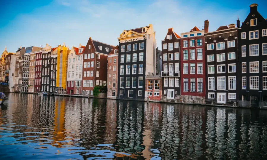 Canal row houses reflecting in water along historic waterfront with moored boat.