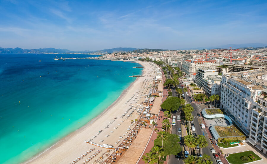 Panoramic view of Cannes, showcasing the beach, Promenade de la Croisette, and the Mediterranean Sea in a luxury resort setting.