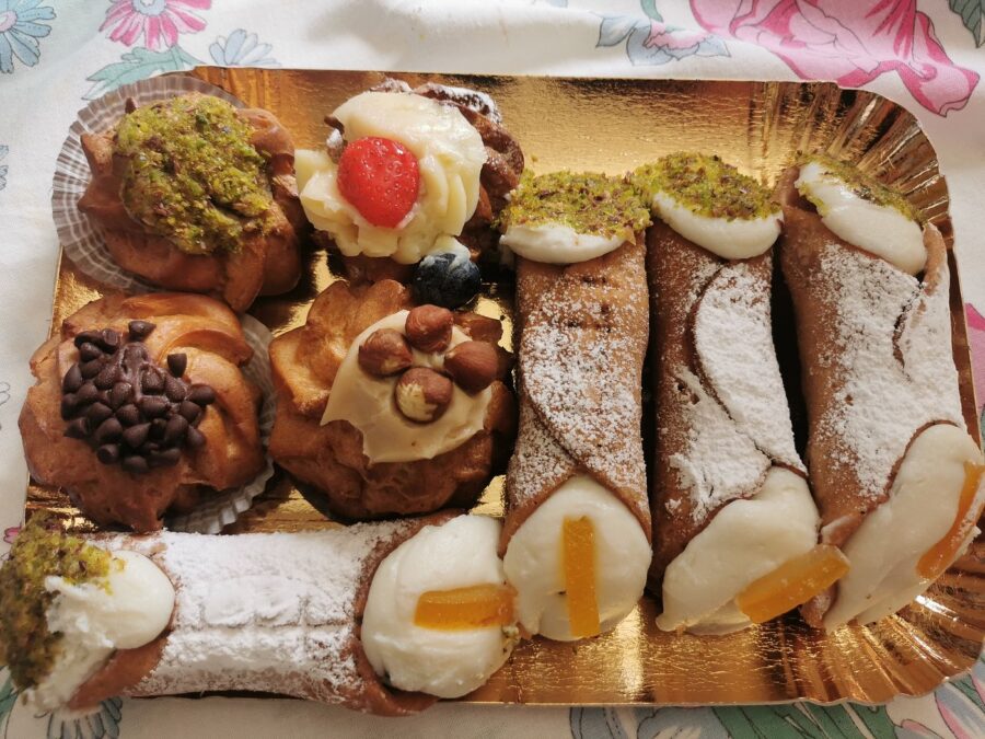 Sicilian cannoli and cream puffs with pistachio on gold tray.