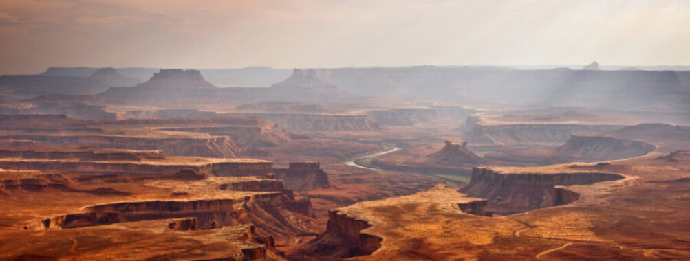Expansive view of Canyonlands National Park in Utah, showcasing rugged canyons and colorful rock formations under a clear sky.