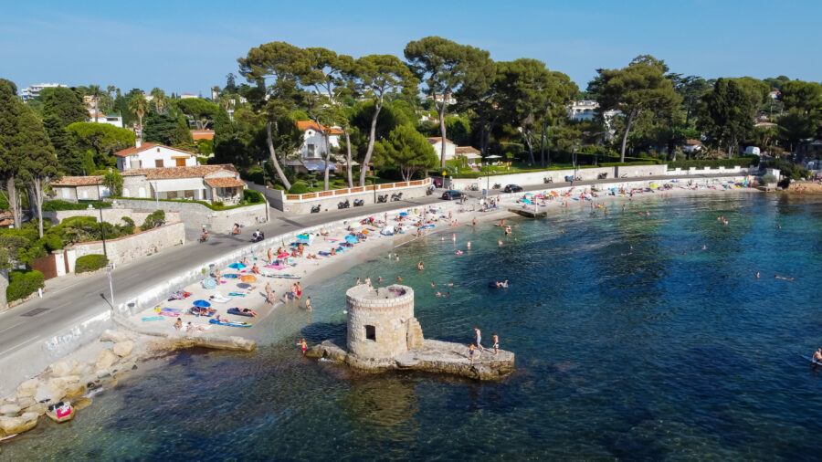 Aerial view of Ondes Beach, Cap d'Antibes, featuring a flooded round watch tower in the Mediterranean Sea.