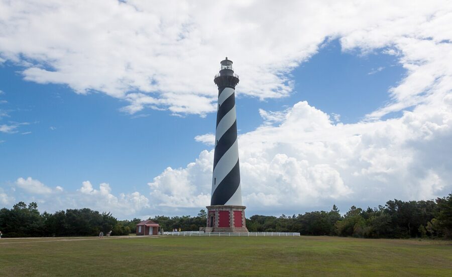 Cape Hatteras Lighthouse, a tall black and white lighthouse with a striking red stripe, stands against a clear sky.