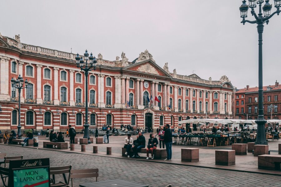 Toulouse Capitole square with neoclassical facade, outdoor cafes, and market stalls.