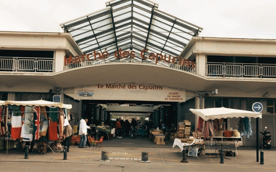 Entrance to bustling Marché des Capucins market with glass roof and diverse international stalls.