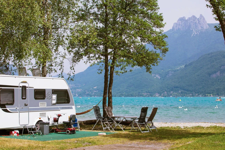 Lakeside caravan campsite with turquoise lake, mountain views, hammock, and camping chairs.