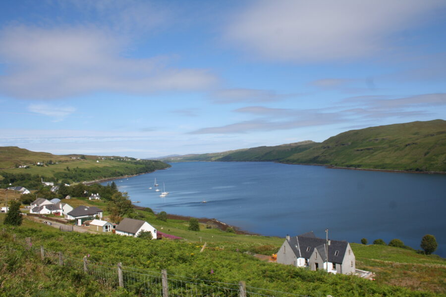 Scenic view of Carbost, Isle of Skye, featuring a tranquil lake surrounded by a few houses.
