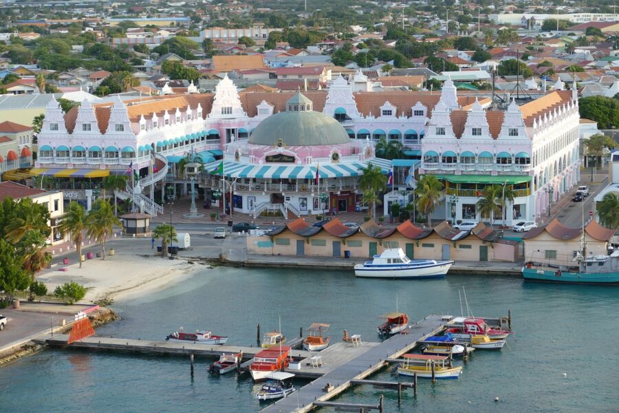Caribbean waterfront with colorful buildings, vibrant marina, palm trees, sandy beach, and sunset glow.