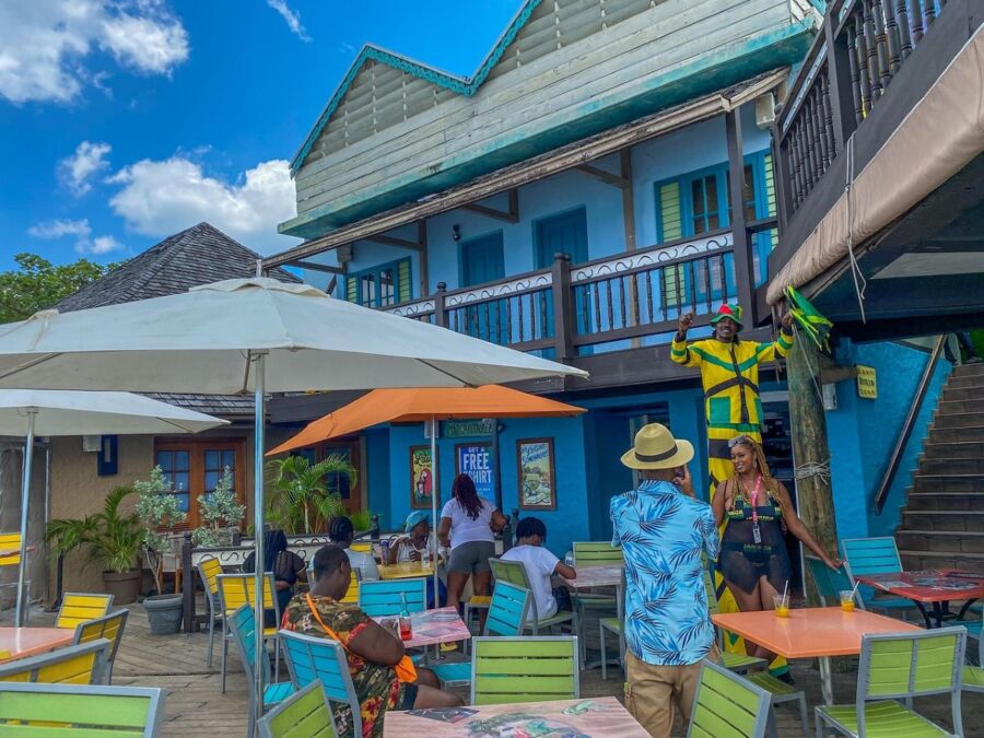 Tropical café scene with colorful seating, lively guests, in a vibrant island setting.