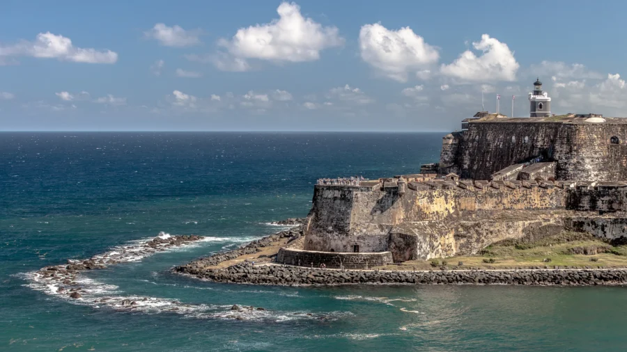 Caribbean coastal stone fortress with lighthouse overlooking turquoise ocean and blue sky.