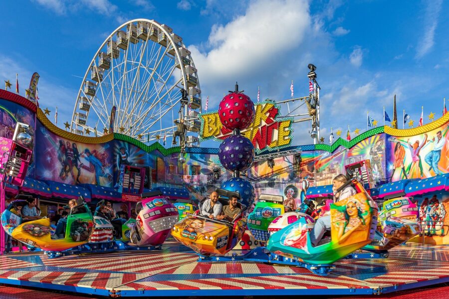 Amusement park break dance ride with colorful spinning cars and Ferris wheel in background.