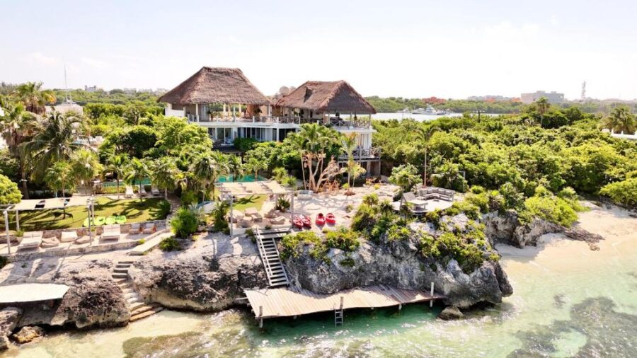 Casa Coco, a beach house in Isla Mujeres, Mexico, surrounded by lush trees and rugged rocks, creating a tranquil atmosphere.
