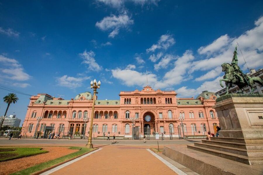 Casa Rosada in Buenos Aires with blue sky, palm trees, and a historic mounted statue.
