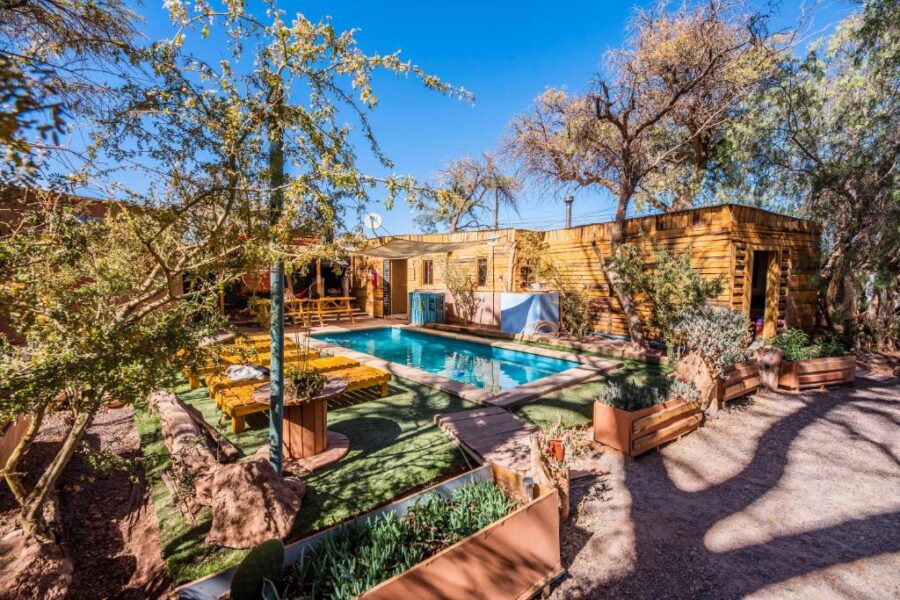 The backyard of Casa Voyage Hostel showcases a refreshing pool and vibrant trees in San Pedro de Atacama, Chile.
