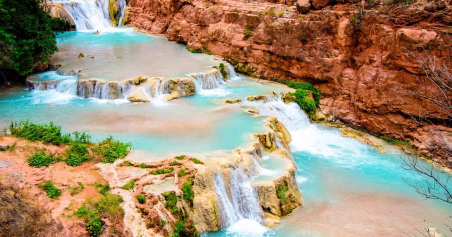Turquoise waterfalls cascade over rocky cliffs with lush greenery.