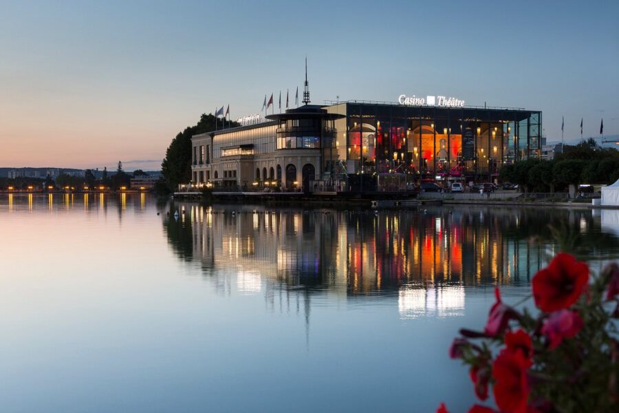 Casino de Théâtre mirrored on calm water at sunset with vibrant garden flowers.