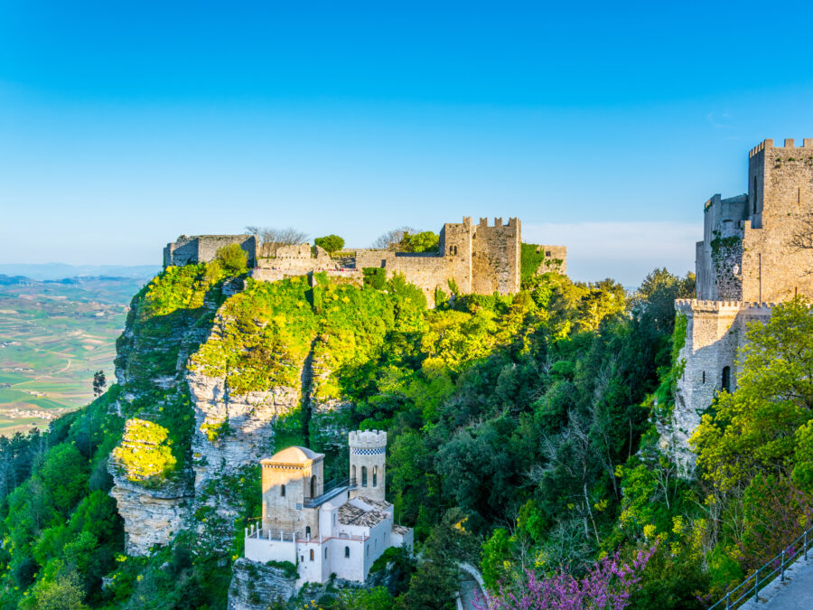 Scenic view of Castello di Venere, a historic castle in Erice, Sicily, surrounded by lush greenery and blue skies.