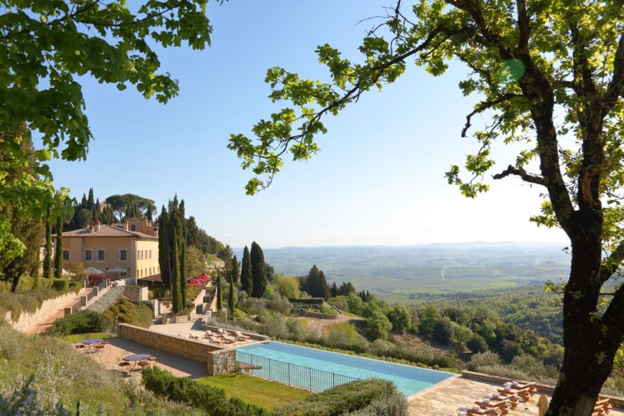 Luxurious Tuscan resort with terracotta architecture, pool, cypress trees, and vineyard views.
