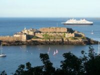 Distant view of a large ship near Castle Cornet, Guernsey, with the historic castle prominently featured.