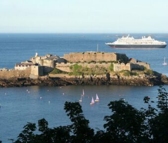 Distant view of a large ship near Castle Cornet, Guernsey, with the historic castle prominently featured.