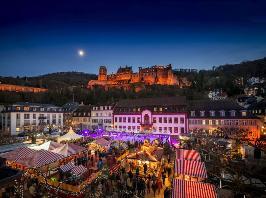 Heidelberg Christmas market at night with illuminated castle and festive stalls.
