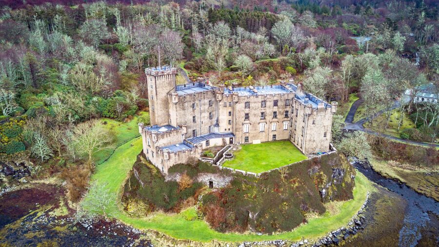 Stone castle on a hill surrounded by lush greenery and a waterway.