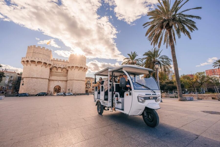 Sunlit castle, eco-friendly vehicle, palm trees, tourists, historical architecture, vibrant public square.