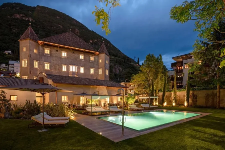 Luxury Bolzano castle hotel courtyard with illuminated pool at evening.