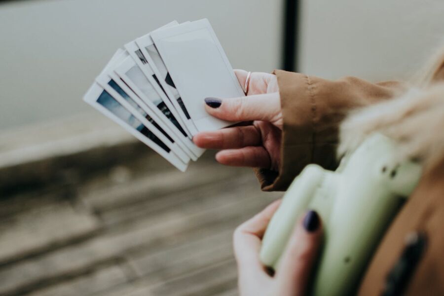 Person holding instant photographs and a retro camera, evoking nostalgia and style.