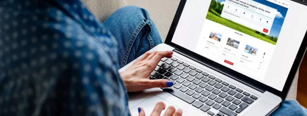 Person booking travel online on a laptop, seated on a cozy couch.