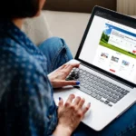 Person booking travel online on a laptop, seated on a cozy couch.