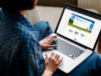 Person booking travel online on a laptop, seated on a cozy couch.