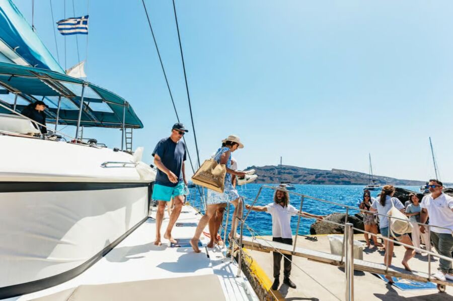 Passengers aboard a catamaran sailing in the ocean, surrounded by a vibrant blue sky during a Santorini experience.