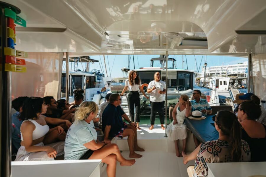 Passengers on a catamaran deck engaged in conversation with a man during a sailing cruise experience in Santorini.