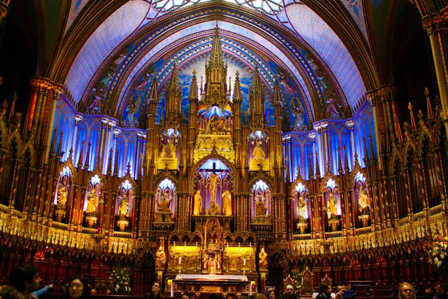 Ornate Gothic church interior with statues, golden altar, arches, frescoes, and stained glass windows.
